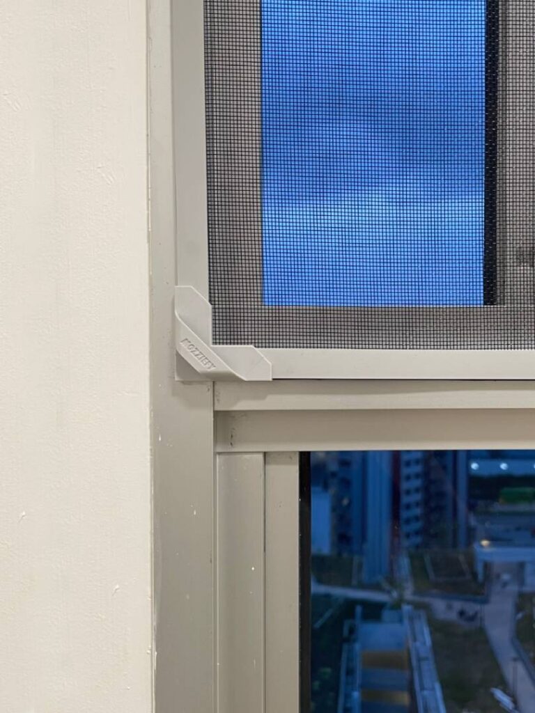 Close-up of a magnetic insect screen securely installed on a white window frame in a Singapore apartment, showing fine insect mesh and corner fastening.
